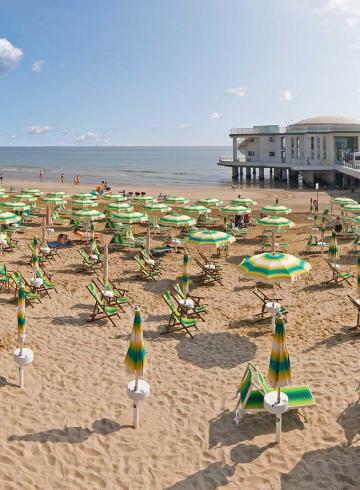 Spiaggia con ombrelloni verdi e edificio sul mare.