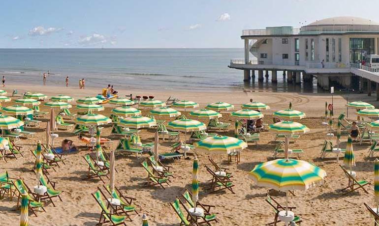 Spiaggia con ombrelloni verdi e edificio sul mare.