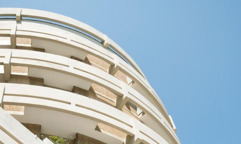 Edificio moderno con balconi curvi e fiori rosa sotto un cielo azzurro.