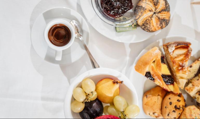 Colazione con caffè, frutta, pane e dolci assortiti.