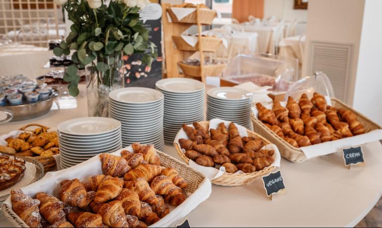 Buffet di croissant e dolci con piatti e rose bianche.