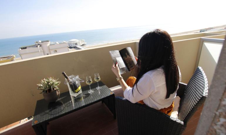 Donna legge in terrazza con vista mare, vino e rivista.