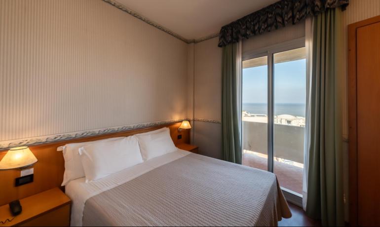 Camera d'albergo con vista mare, letto matrimoniale e lampade accese.