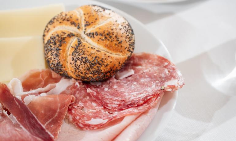 Colazione con salumi, formaggio, pane e dolci assortiti.