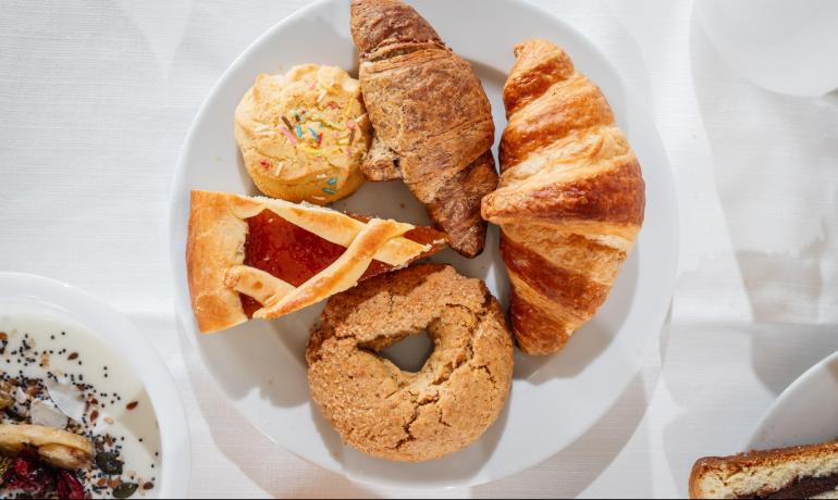 Piatto con croissant, biscotti e crostata su tovaglia bianca.