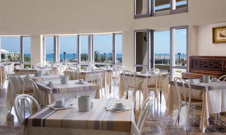 Ristorante luminoso con vista mare e tavoli apparecchiati.