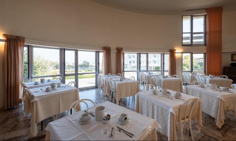 Sala da pranzo luminosa con tavoli apparecchiati, finestre panoramiche.