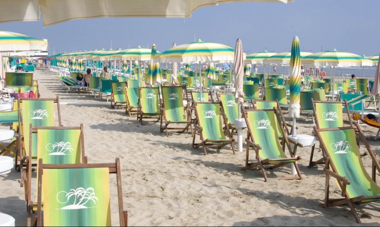 Spiaggia sabbiosa con lettini e ombrelloni colorati sotto il sole.