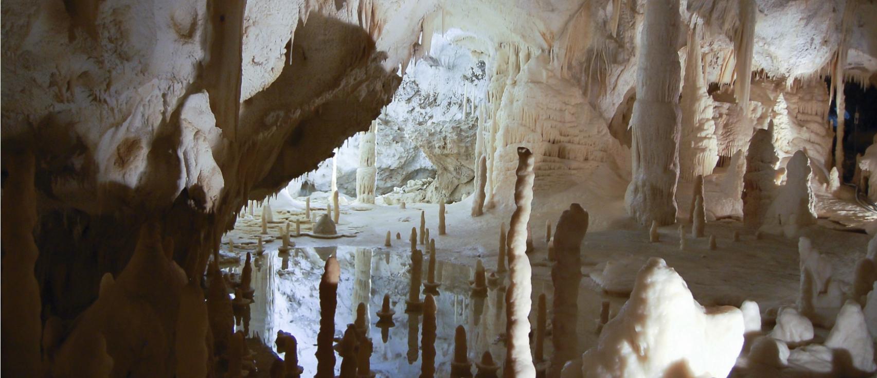 Caverna con stalattiti e stalagmiti riflessi in acqua cristallina.