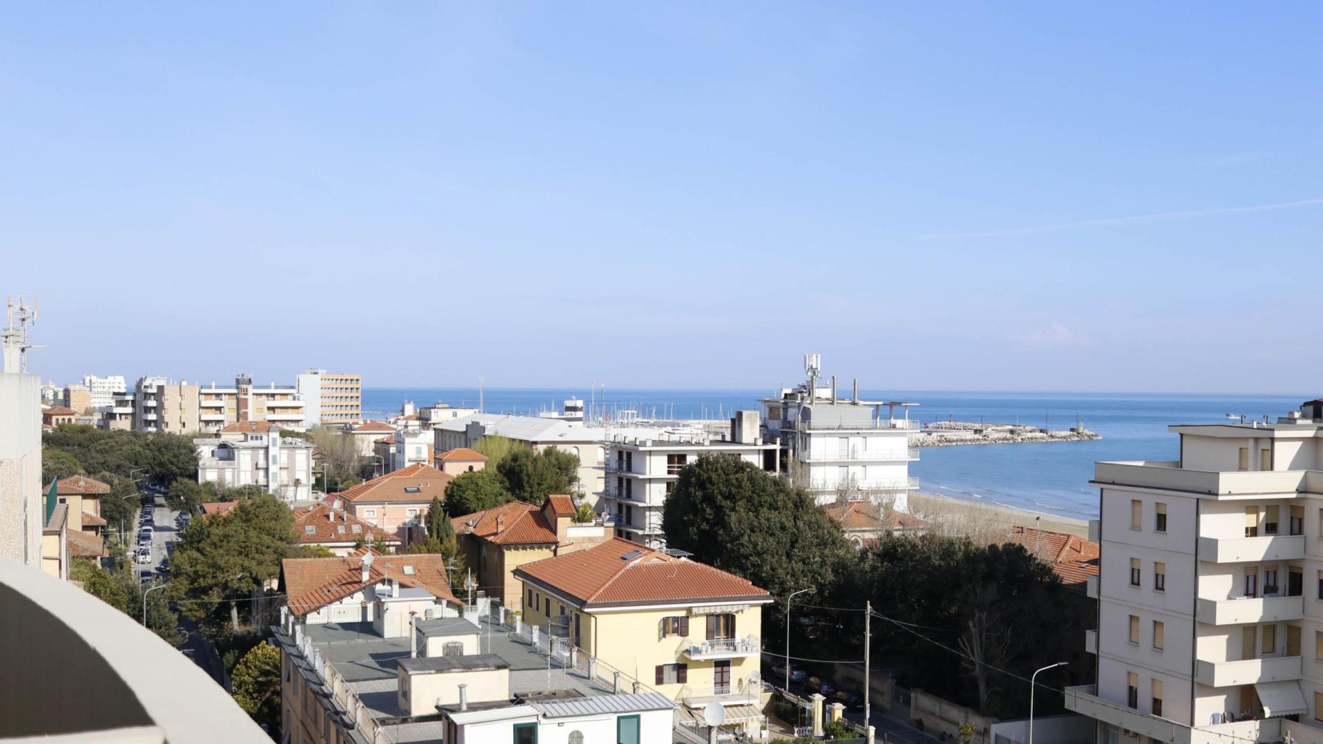 Vista urbana con edifici, tetti rossi e mare sullo sfondo.