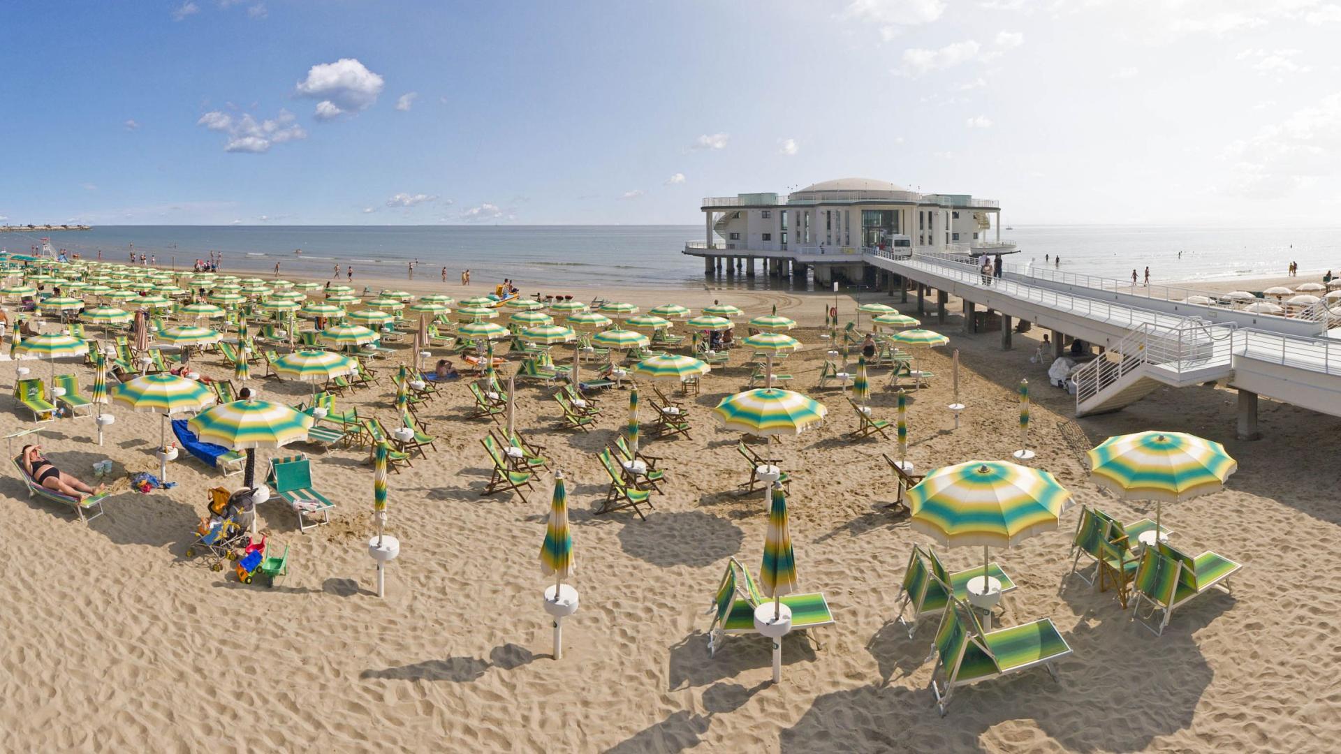 Spiaggia con ombrelloni colorati e struttura sul mare, giornata soleggiata.