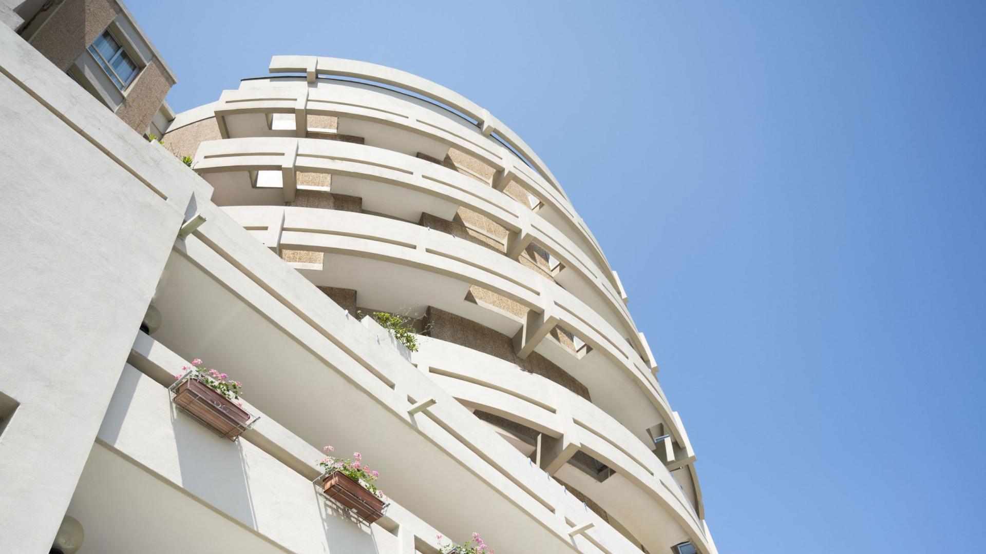 Edificio moderno con balconi curvi e fioriere, cielo azzurro sullo sfondo.