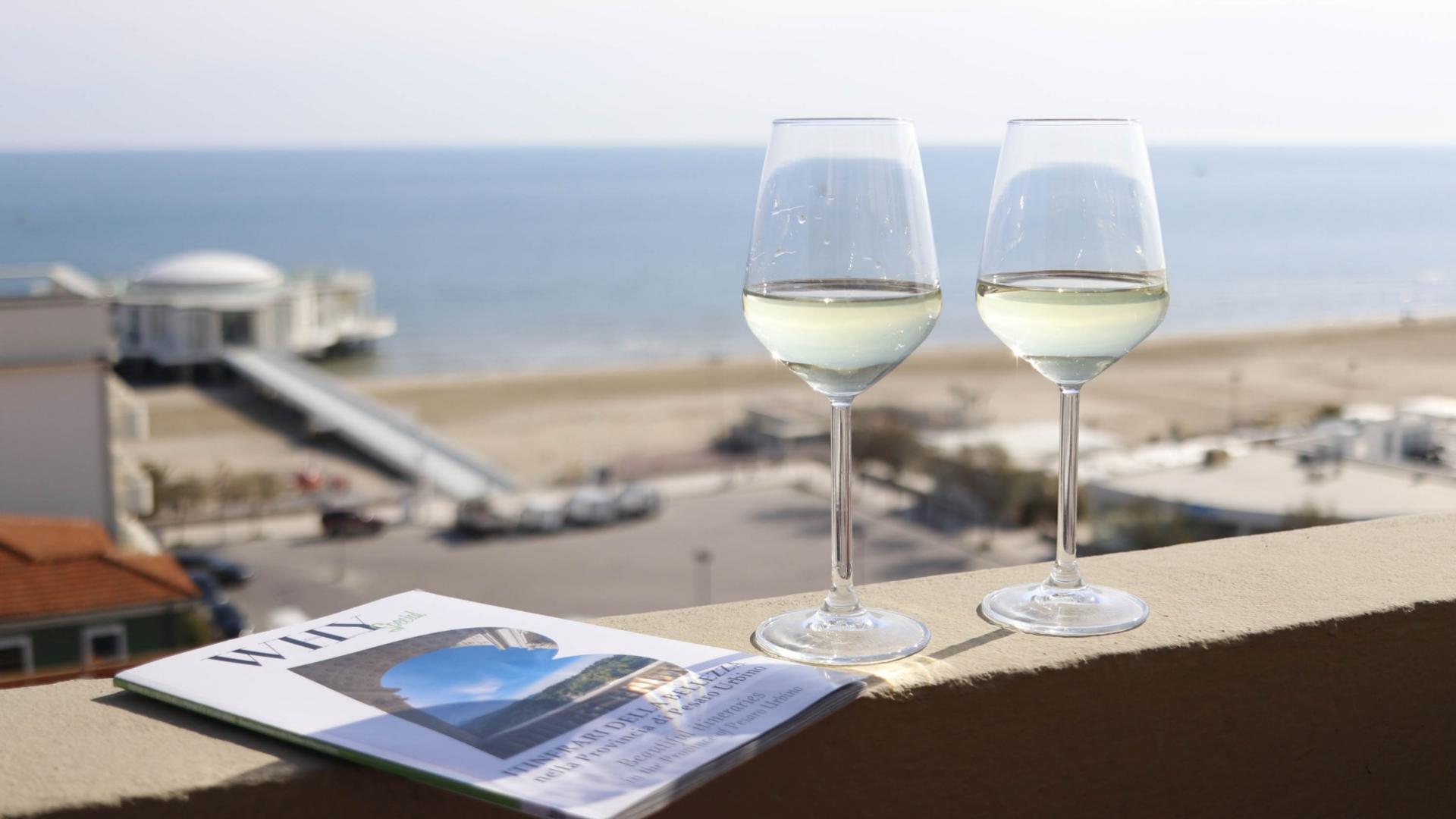 Due calici di vino bianco con vista mare e un opuscolo sulla ringhiera.