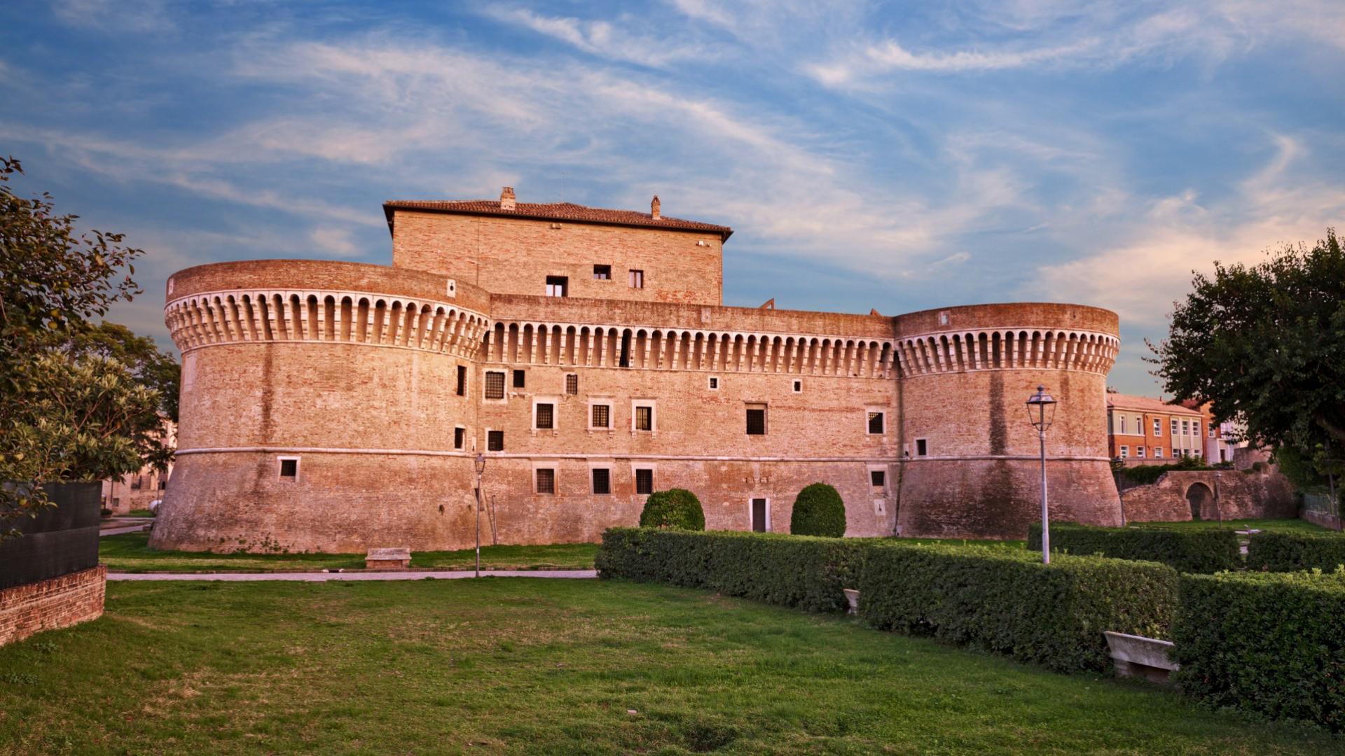 Imponente fortezza medievale con torri circolari e mura in mattoni al tramonto.