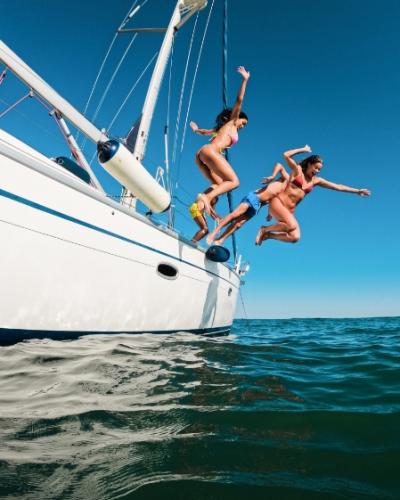 Persone che si tuffano in mare da una barca a vela in una giornata soleggiata.