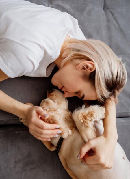 Donna abbraccia un cane su un divano grigio, mostrando affetto e tenerezza.