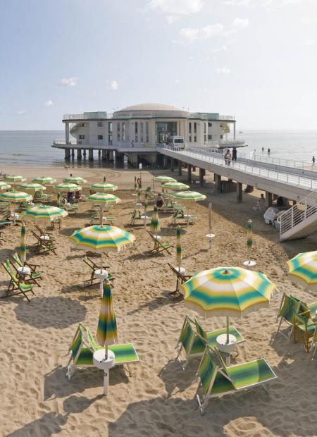 Spiaggia con ombrelloni colorati e un edificio su palafitte sul mare.