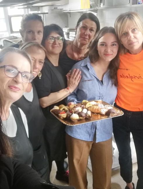 Gruppo di donne in cucina con vassoio di dolci e sorrisi.