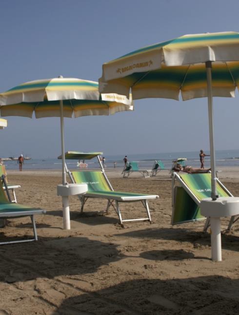 Spiaggia con ombrelloni e lettini, persone sullo sfondo vicino al mare.