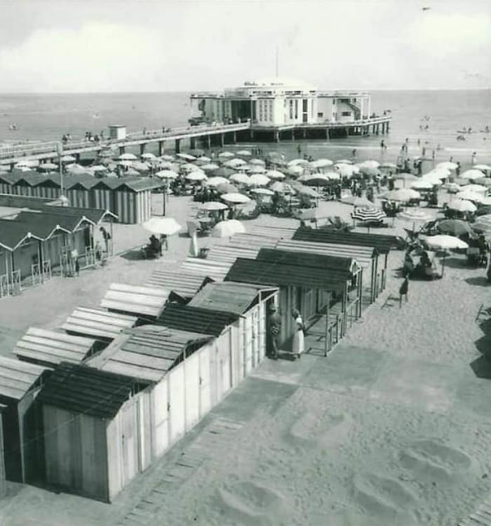 Spiaggia con cabine e ombrelloni, vista su un edificio sul mare.