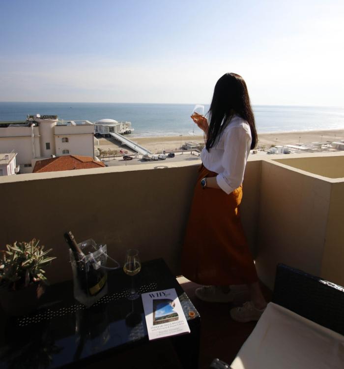 Donna su terrazza vista mare con bicchiere di vino, atmosfera rilassante.