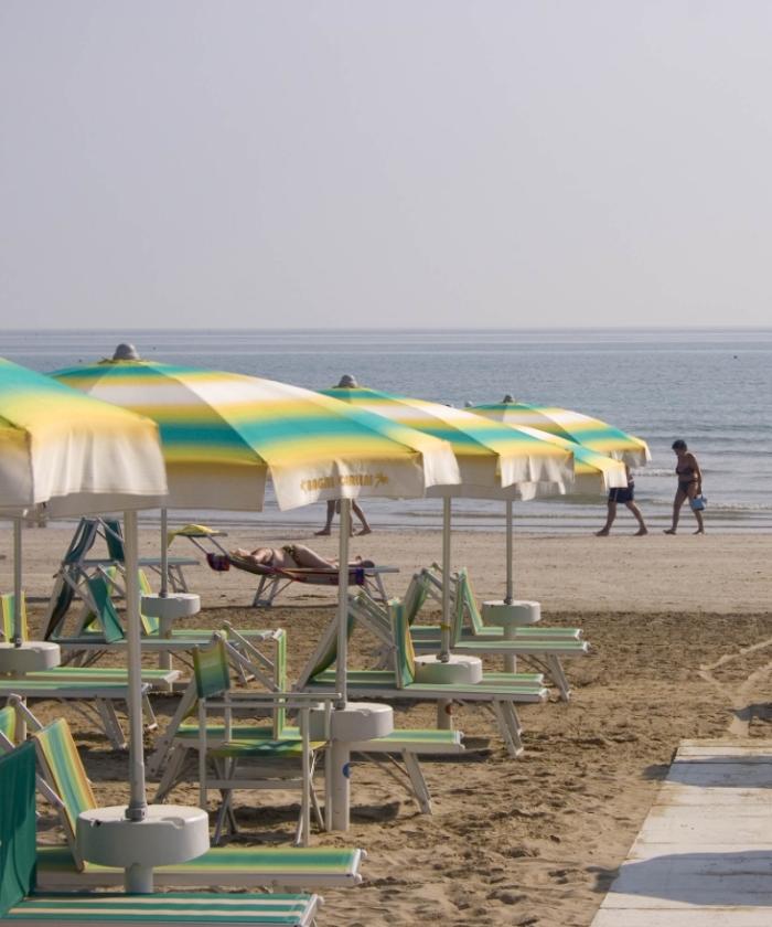 Spiaggia con ombrelloni colorati e persone che passeggiano lungo il mare.