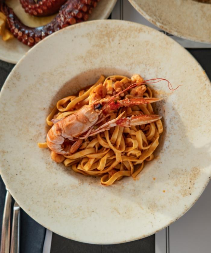 Tagliatelle ai frutti di mare con scampo, in piatto rustico.