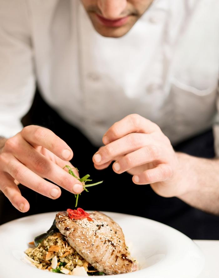 Chef prepara un piatto raffinato con pesce e verdure, aggiungendo guarnizioni.