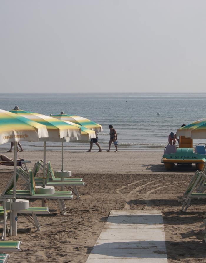 Spiaggia con ombrelloni gialli e verdi, persone camminano sulla riva del mare.