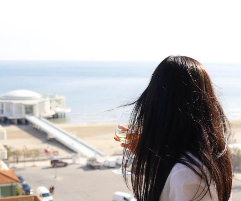 Donna con bicchiere guarda il mare da un balcone.