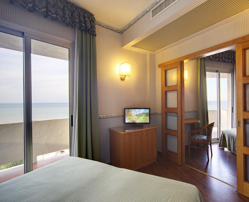 Camera d'hotel con vista mare, TV, letto e porta scorrevole in legno.