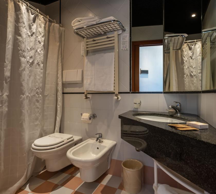 Bagno con doccia, bidet, lavabo, specchio e asciugamani su scaffale.