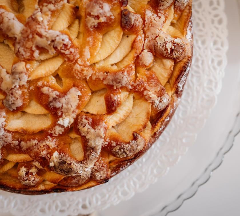 Torta di mele con crosta dorata e zucchero a velo su piatto decorativo.