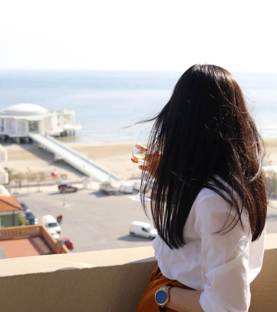 Donna con bicchiere di vino guarda il mare da un balcone soleggiato.