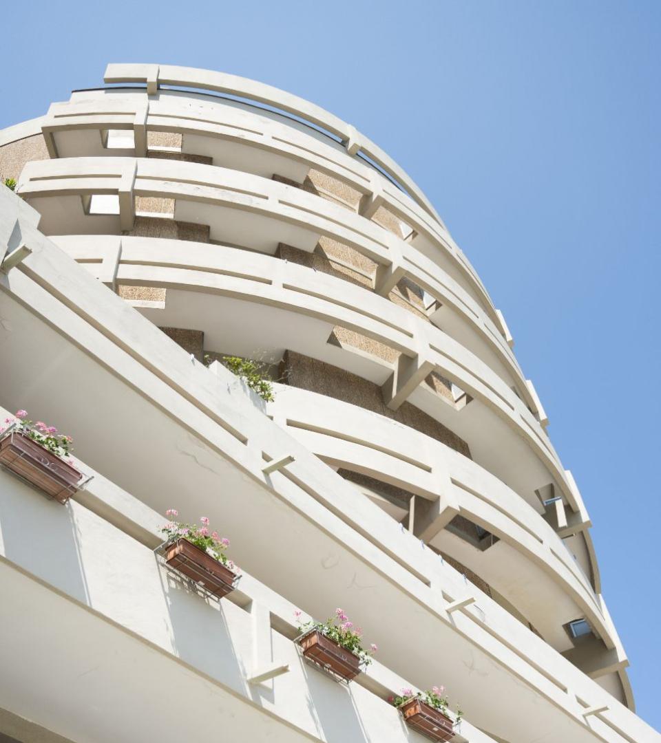 Edificio moderno con balconi curvi e fioriere, cielo azzurro sullo sfondo.