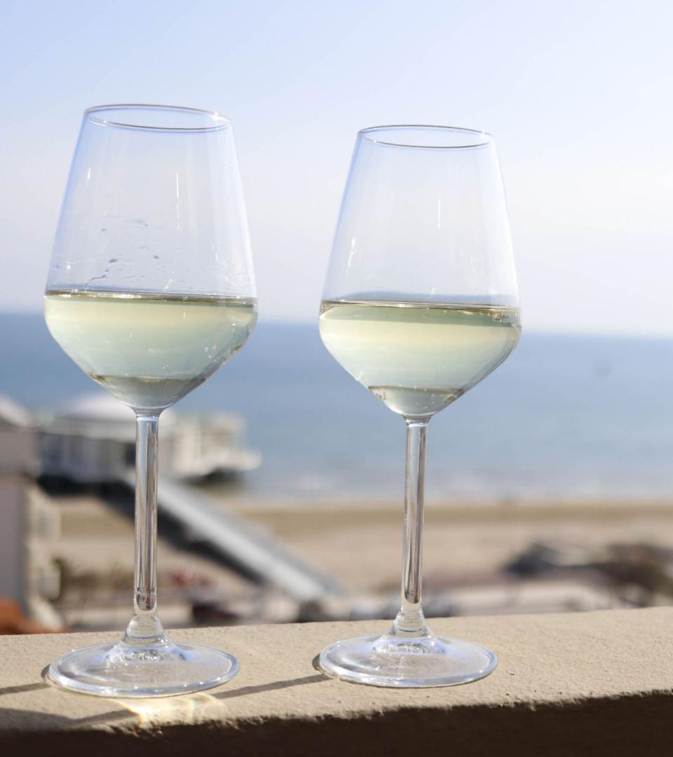 Due bicchieri di vino bianco con vista sul mare in una giornata soleggiata.