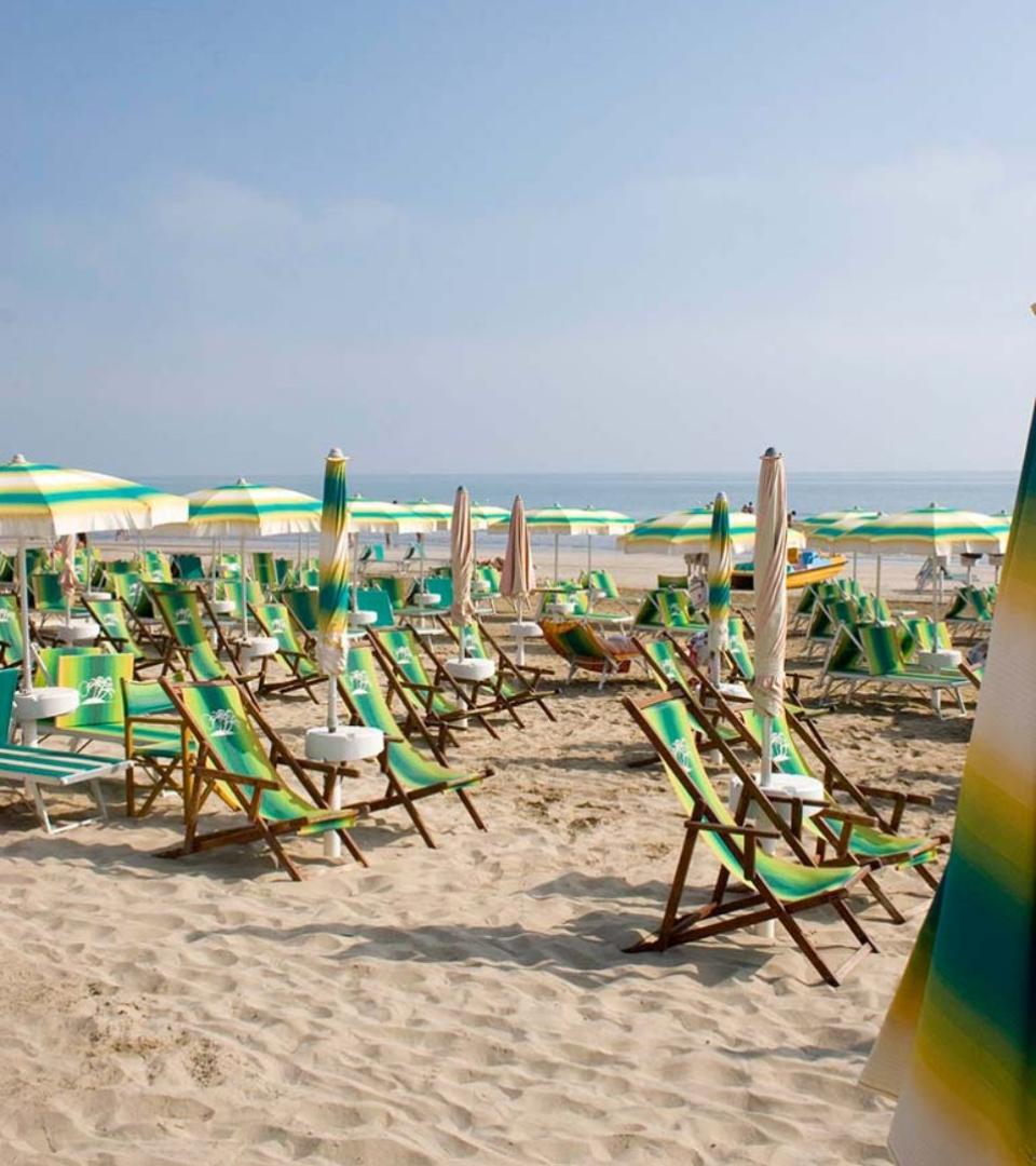 Spiaggia con sedie a sdraio e ombrelloni verdi e gialli, cielo sereno.