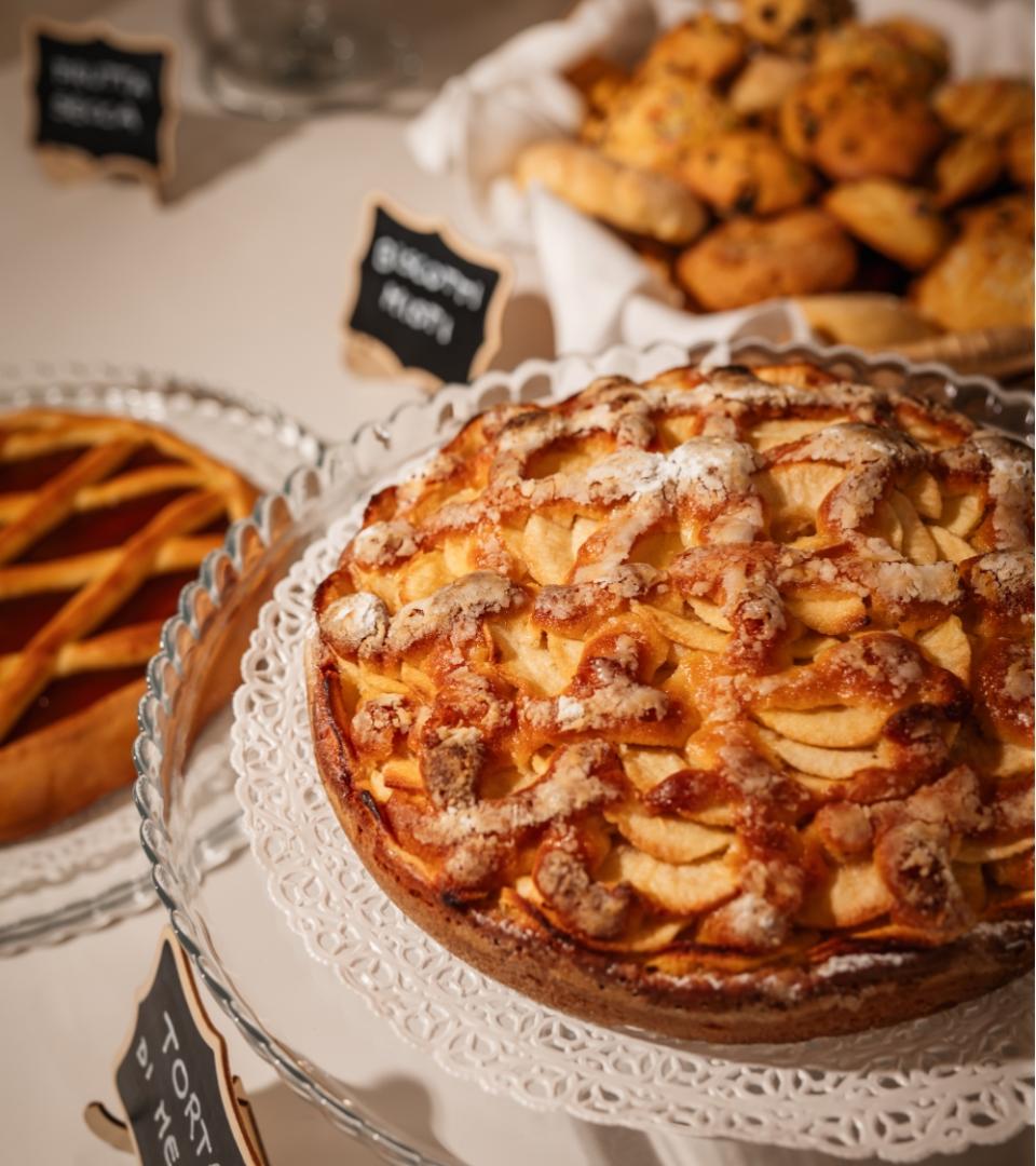 Torta di mele in primo piano, dolci assortiti sullo sfondo su un tavolo.