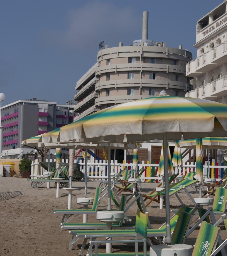 Spiaggia con ombrelloni colorati e edifici moderni sullo sfondo.